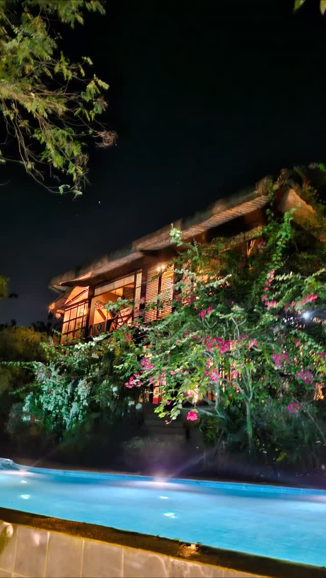 The Red Hen Homestead farmhouse glowing with warm light at night, pink bougainvillea and the pool in the foreground